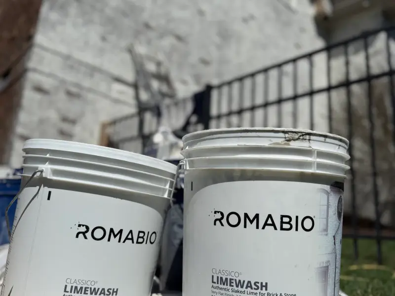 Buckets of Romabio limewash paint in front of a stone house
